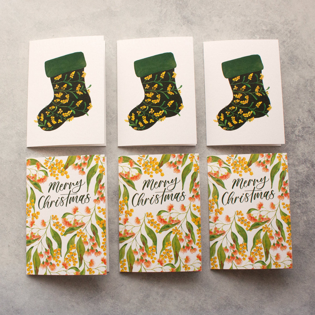 Set of Christmas-themed greeting cards with stockings and floral designs on a grey surface.