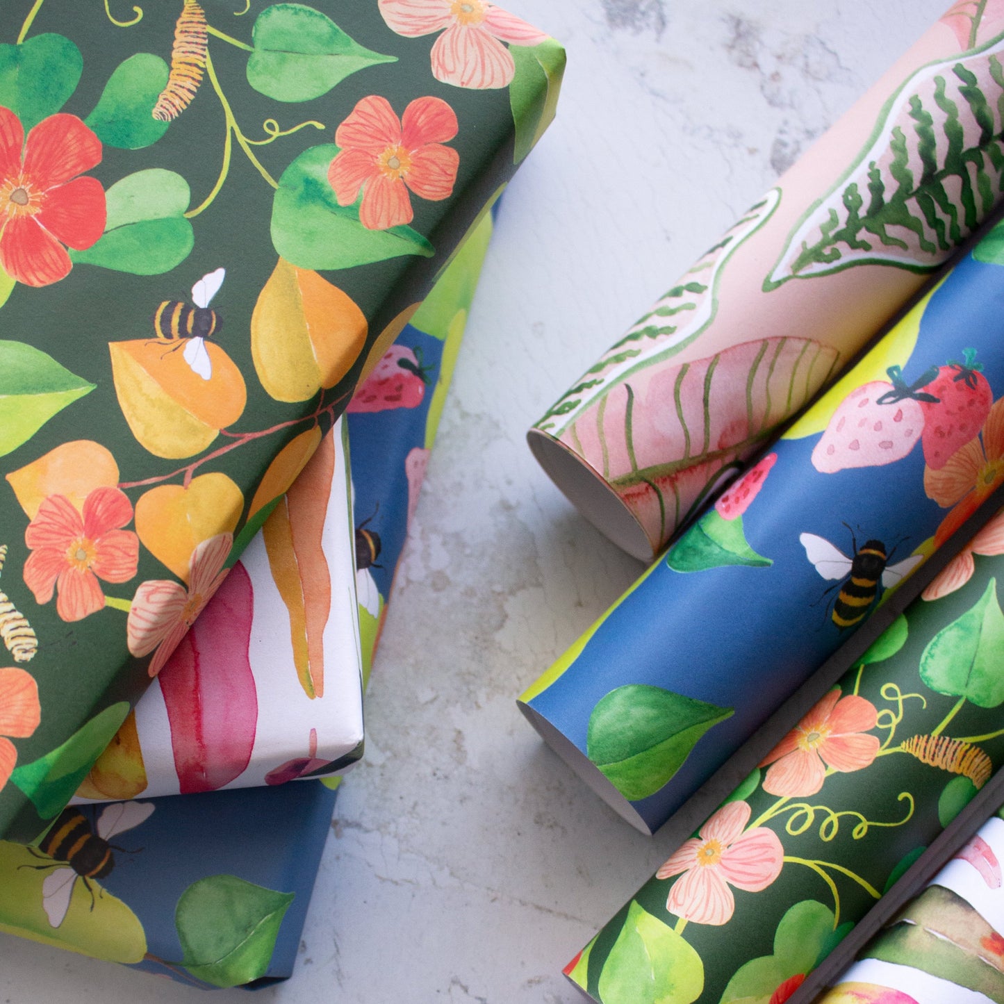 Pile of presents rapped in beautiful hand painted illustrations. Rolls of individual wrapping paper sit next to the pile of presents