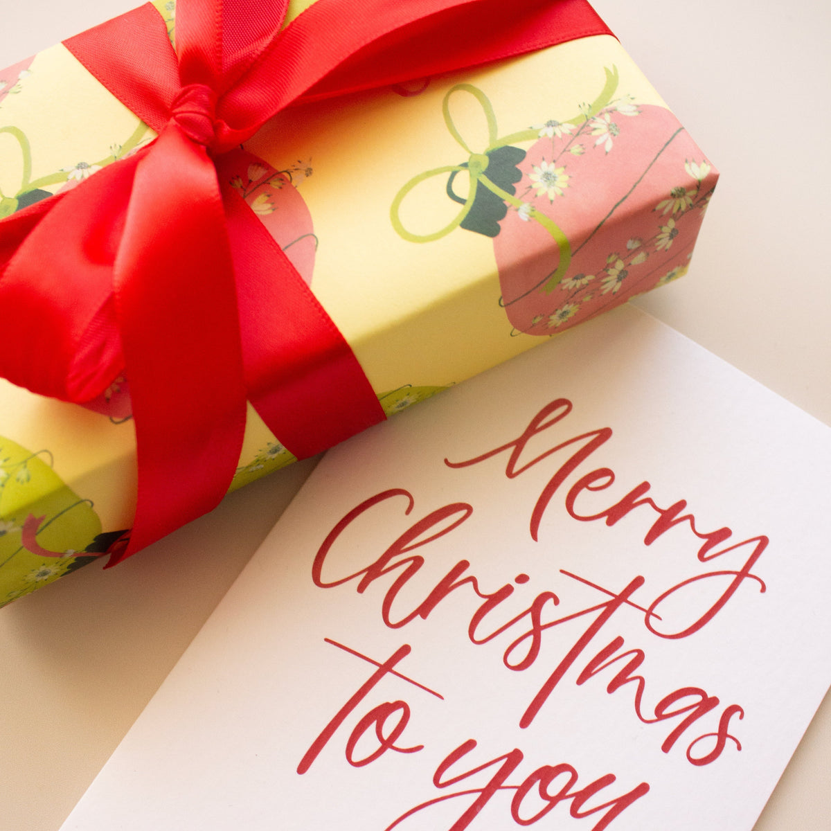 A wrapped gift box with a large red ribbon bow sits beside a white card printed with the words 'Merry Christmas to you' in red script