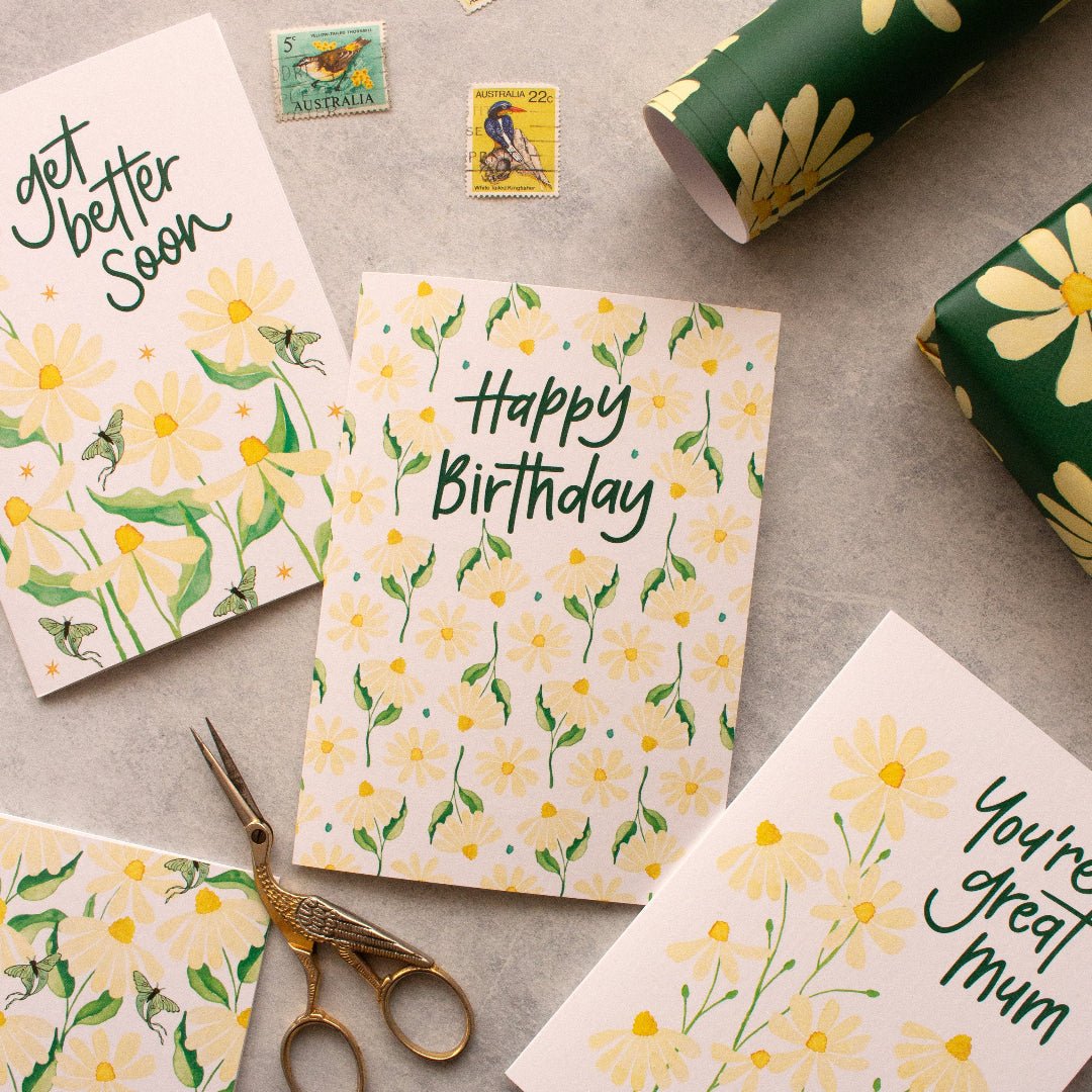 Greeting cards with floral designs and text on a textured surface with stamps and scissors.