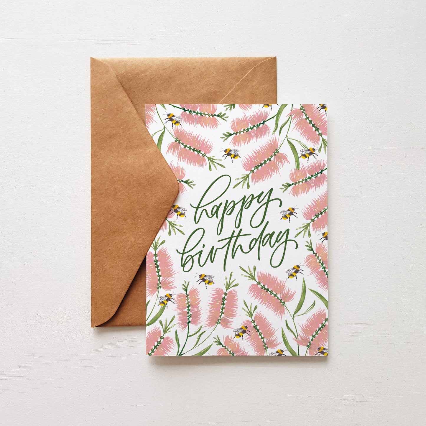 Happy birthday card with pink flowers and bees, brown envelope on a white background