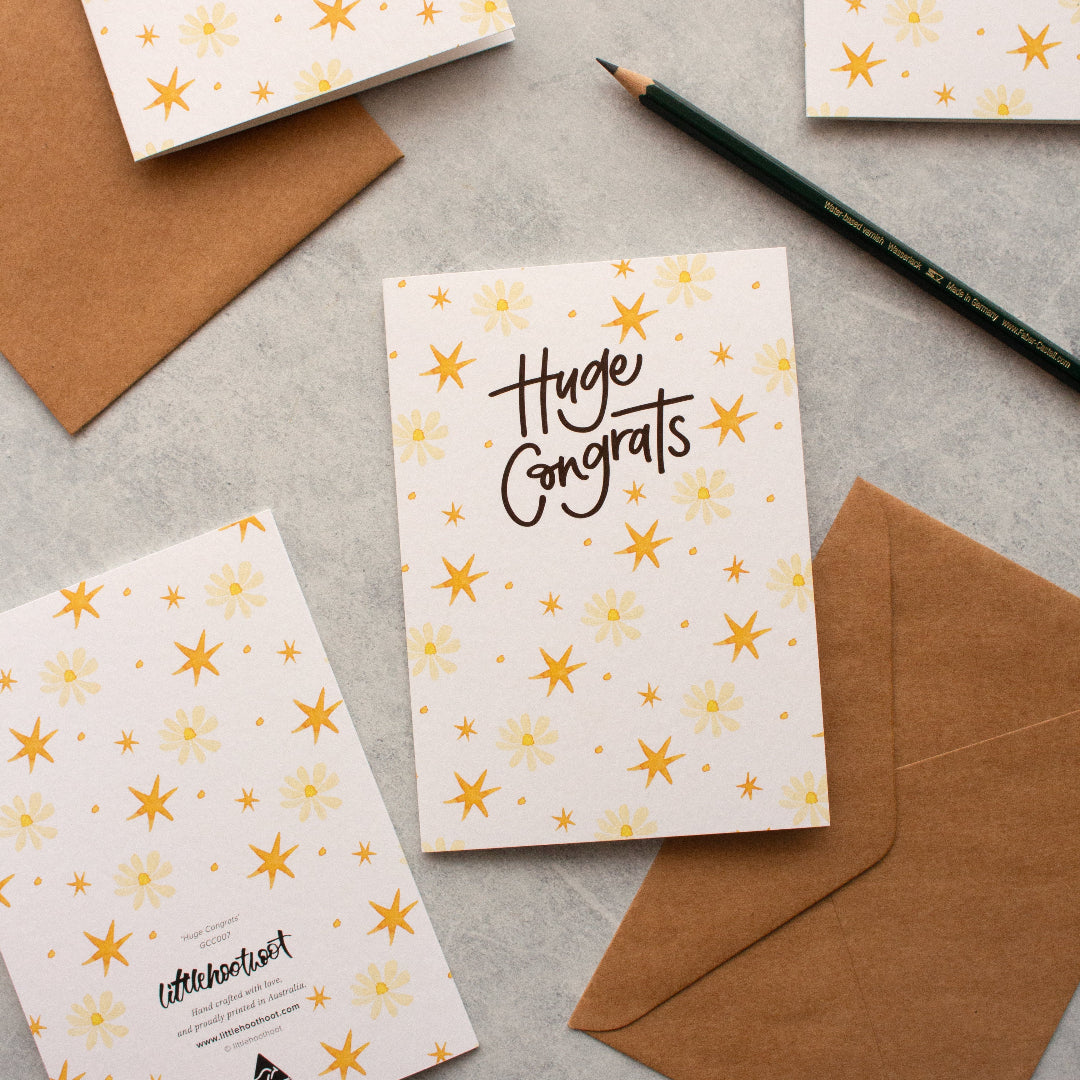 Huge Congrats congratulations card featuring flowers and stars, styled with a pencil and envelopes.