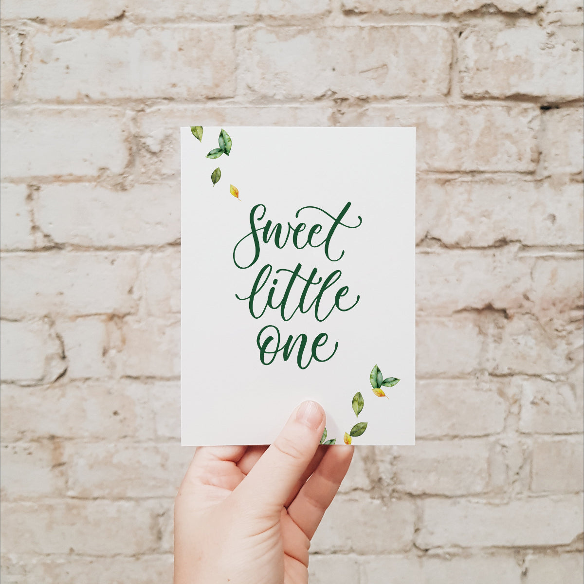Hand holding a botanical baby card with the words 'sweet little one' in green