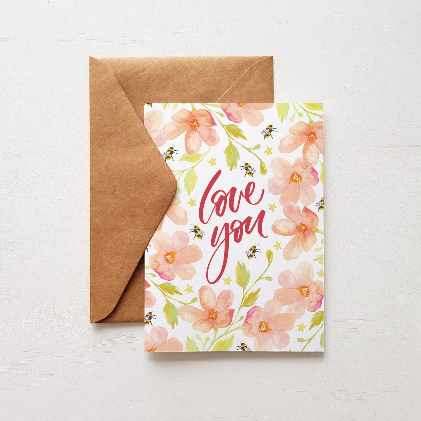 Greeting card with the words 'love you' surrounded by pink flowers. Brown envelope on white background