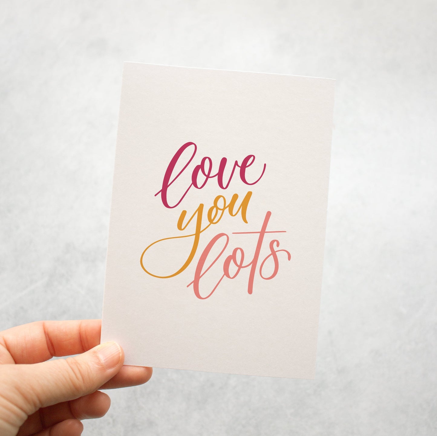 Hand holding a card with 'love you lots' text on a light background