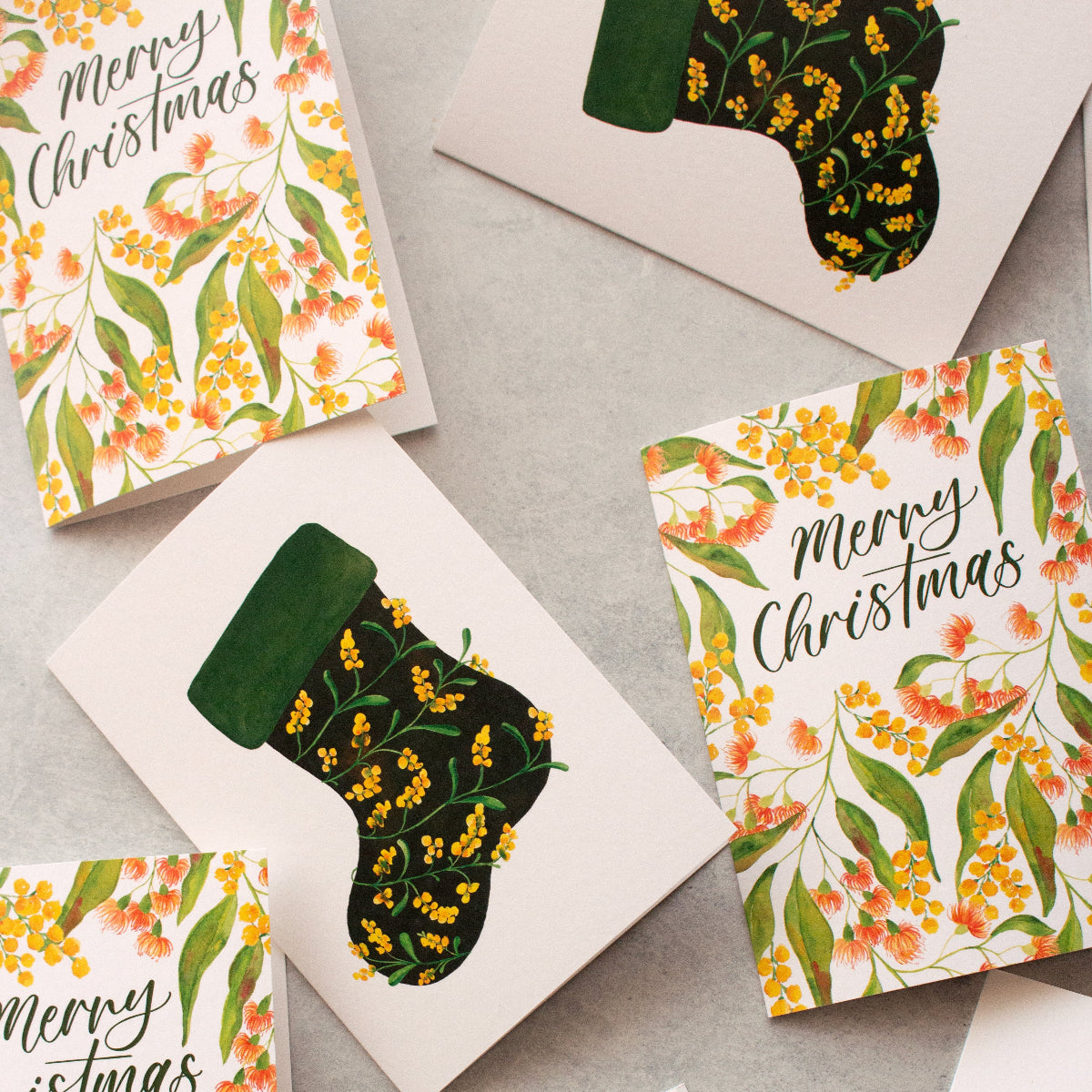 Set of Christmas cards with floral designs and 'Merry Christmas' text on a grey surface.