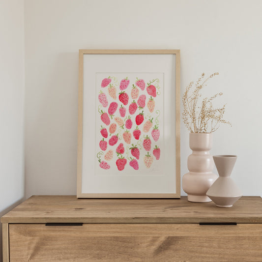 Framed artwork with pink strawberry design on a wooden surface with vases.