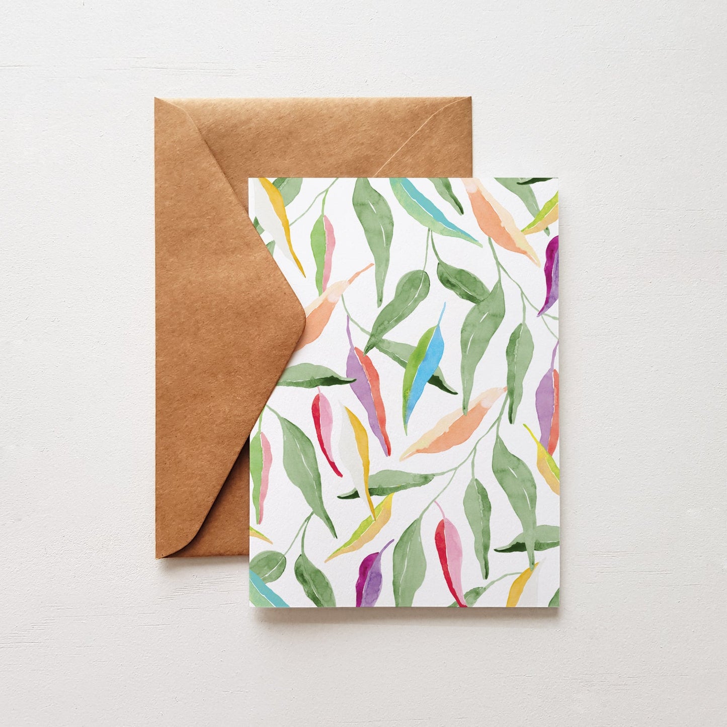 Greeting card with colourful gum leaf pattern and brown envelope on a light gray background