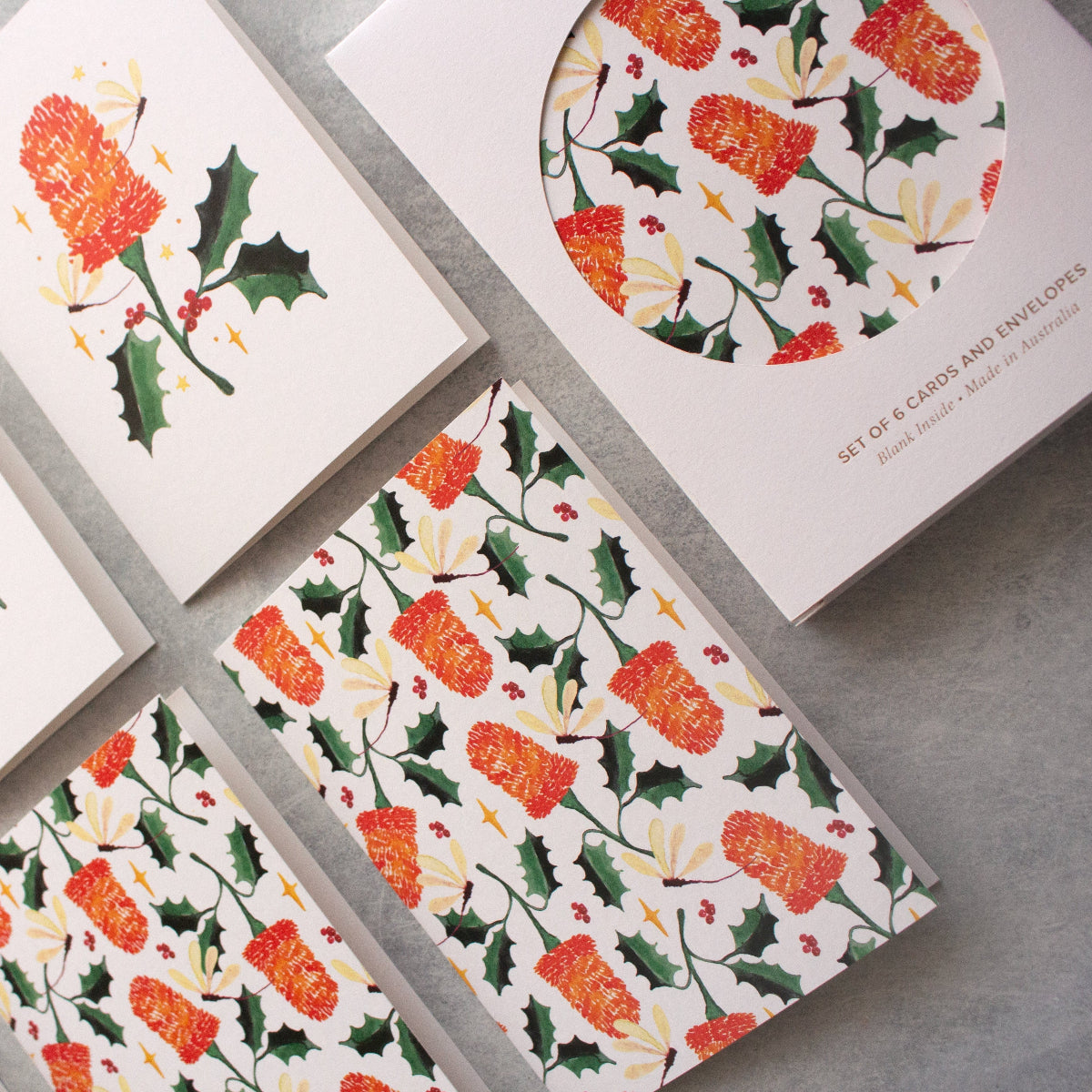 Set of Christmas-themed greeting cards with floral and holly designs on a grey surface.