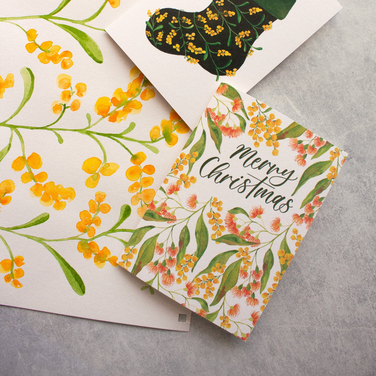 Wattle and flowering gums Christmas card with 'Merry Christmas' text on a grey surface