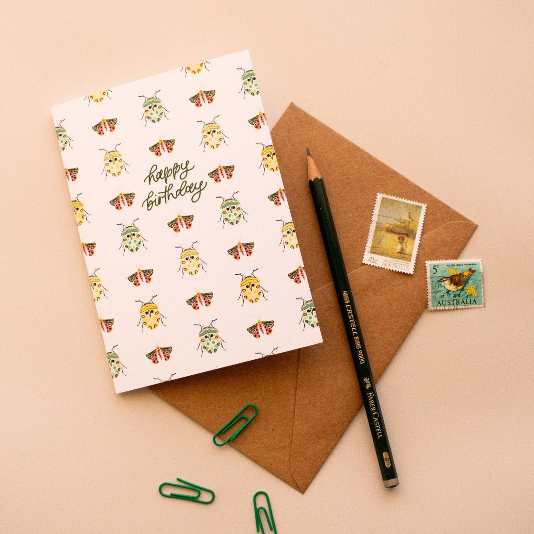 Happy birthday greeting card with a bug pattern on a brown envelope with stamps and a pencil