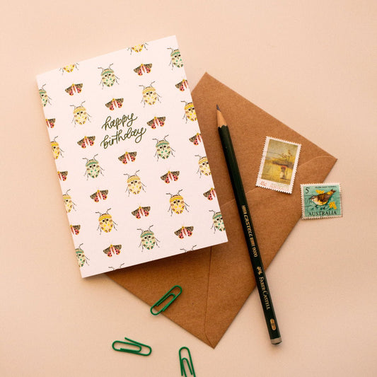 Happy birthday greeting card with a bug pattern on a brown envelope with stamps and a pencil