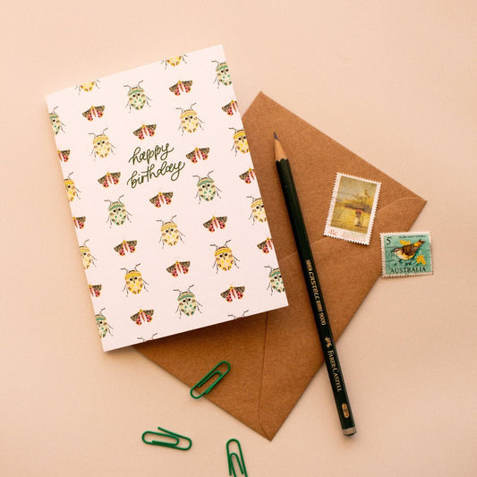 Happy birthday greeting card with a bug pattern on a brown envelope with stamps and a pencil
