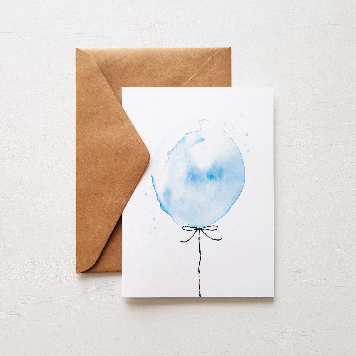 Birthday greeting card with a hand painted blue balloon illustration, accompanied by a brown kraft envelope.