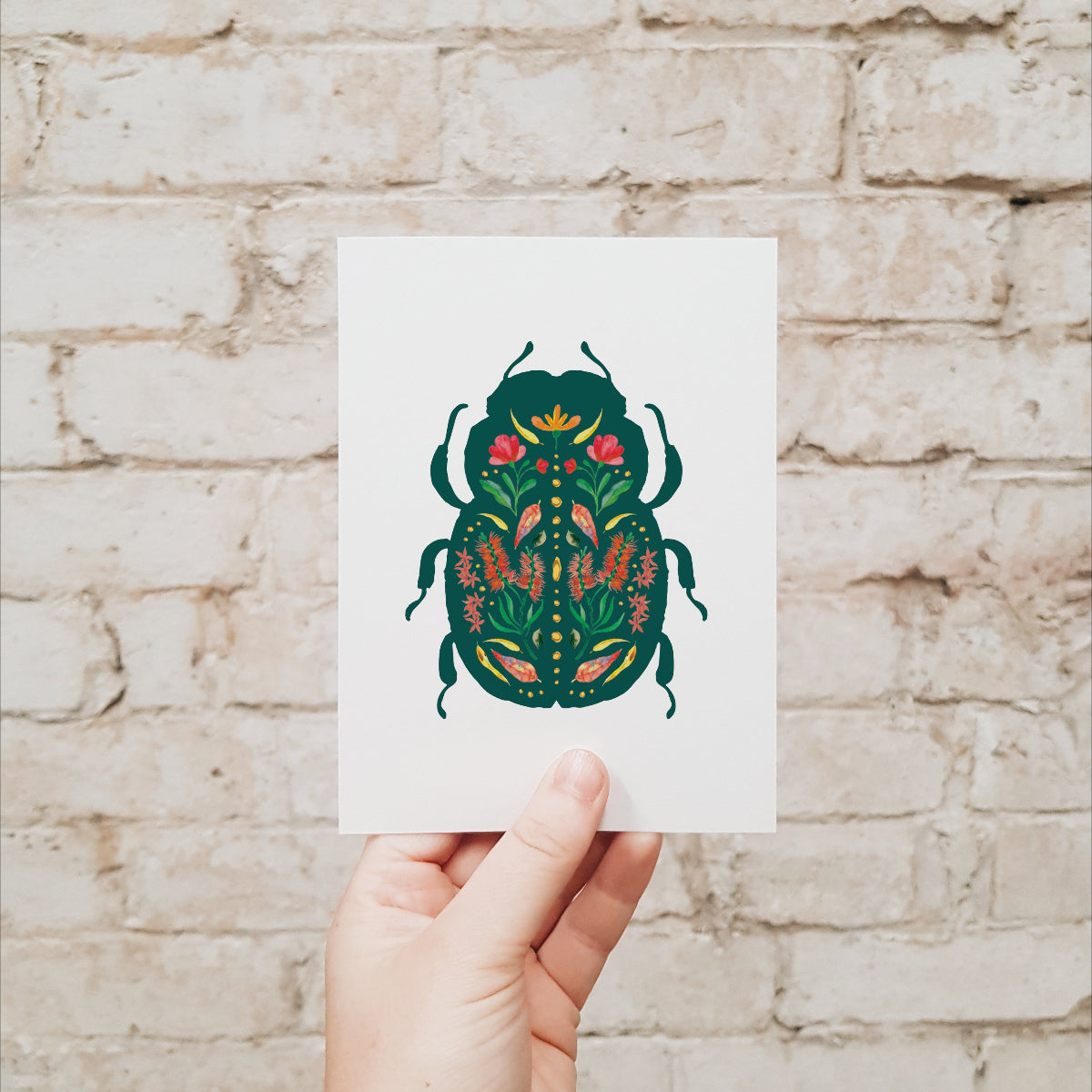Hand holding a card with a beetle design against a brick wall.