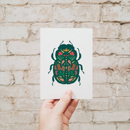 Hand holding a card with a beetle design against a brick wall.