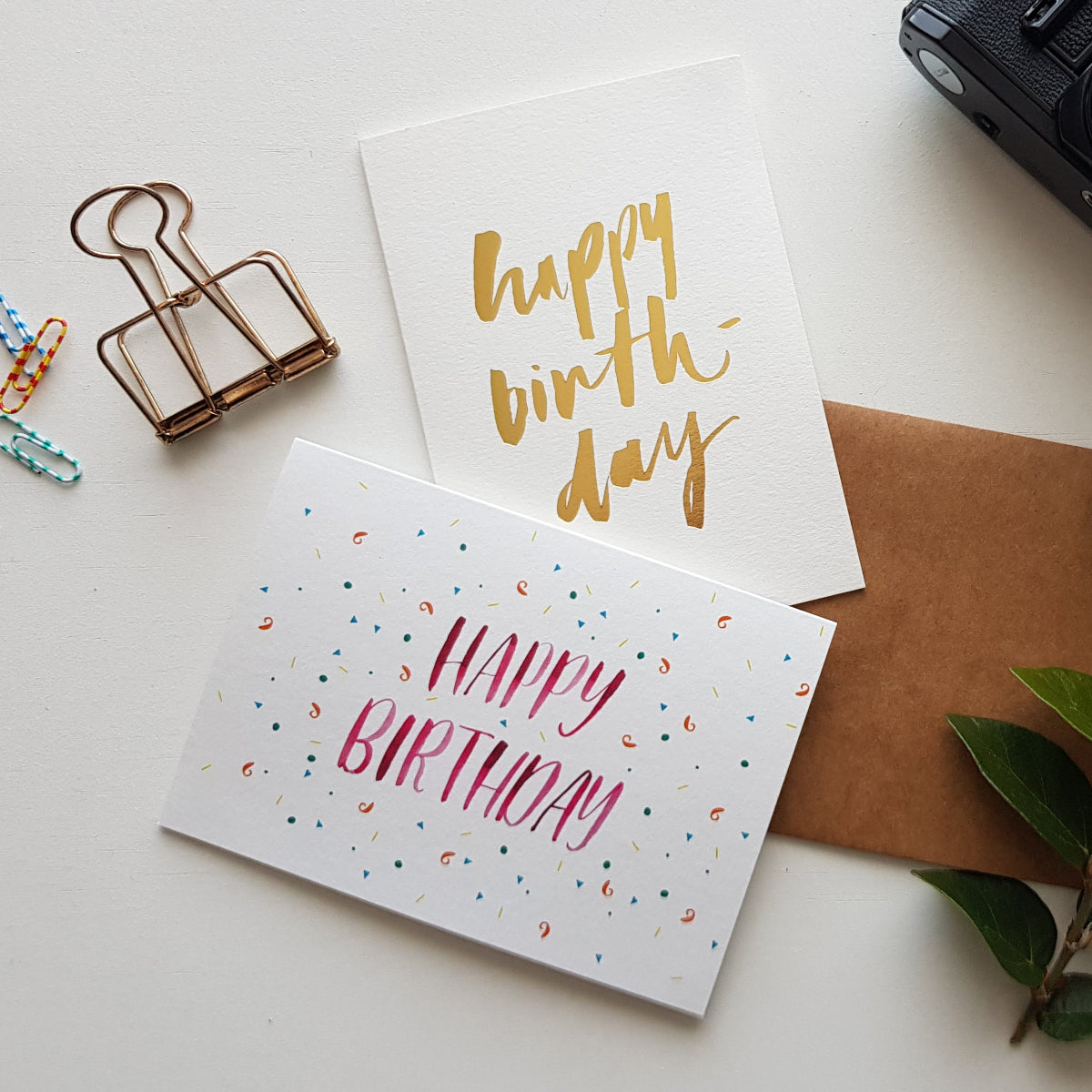 Two happy birthday greeting cards surrounded by stationery