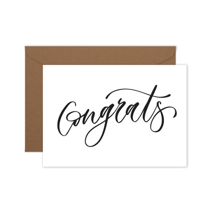 A folded white greeting card with the word 'Congrats' written in a elegant, hand lettered script, and a brown kraft envelope.