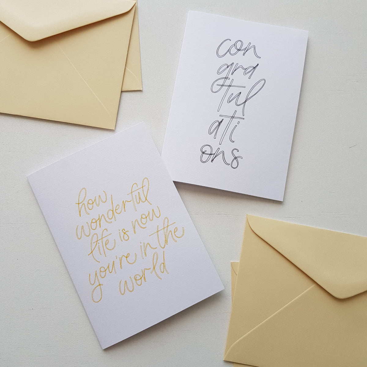 two greeting cards, a baby and a congratulations card with cream envelopes on a white background