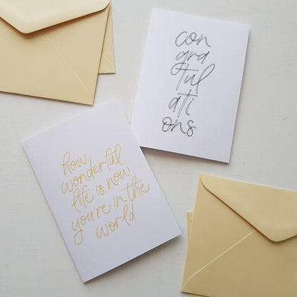 two greeting cards, a baby and a congratulations card with cream envelopes on a white background