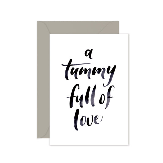 A greeting card with the phrase 'a tummy full of love' written in a cursive script, accompanied by a grey envelope, against a white background.