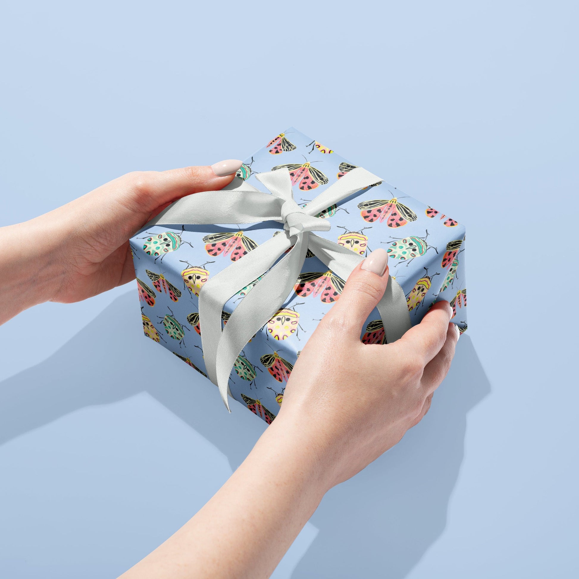 Gift box with floral pattern and white ribbon held by hands against a light blue background