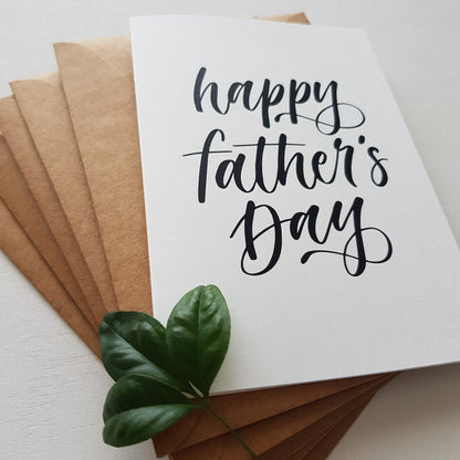close up of father's day greeting card in black script on brown envelopes and a leaf