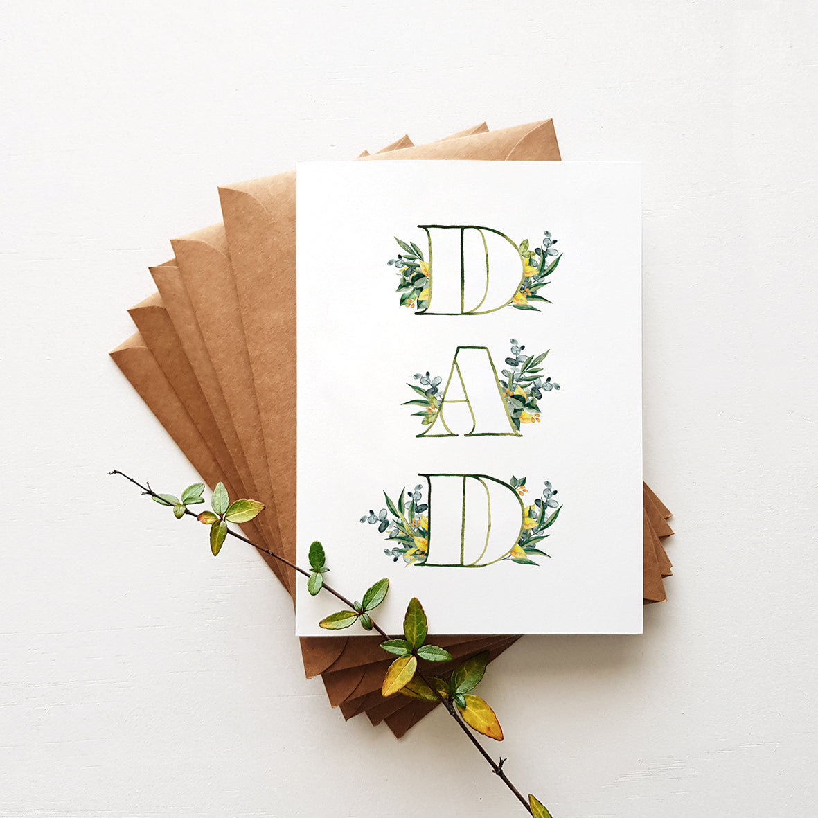 A greeting card with the word 'DAD' surrounded by leaf designs, folded with brown envelopes.
