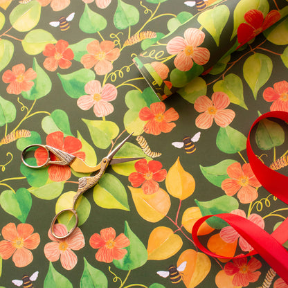 gold bird scissors on a hand painted foliage and floral design. Top right corner sits a roll of wrapping paper and bottom right hand corner a red ribbon