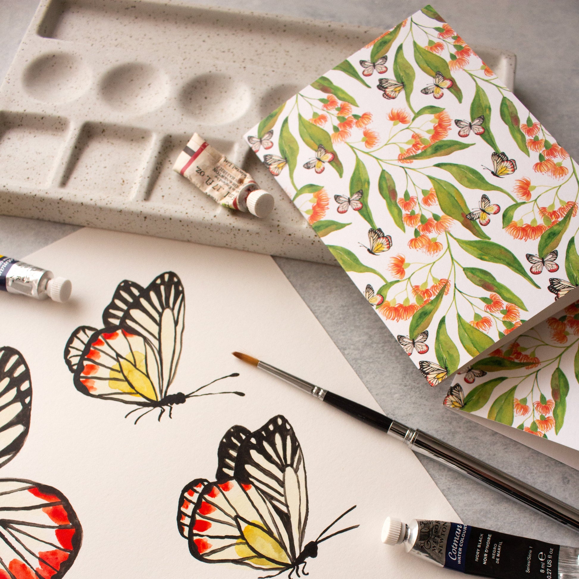 Butterfly illustrations on paper with a paint palette and tubes of paint.