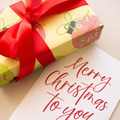 A wrapped gift box with a large red ribbon bow sits beside a white card printed with the words 'Merry Christmas to you' in red script