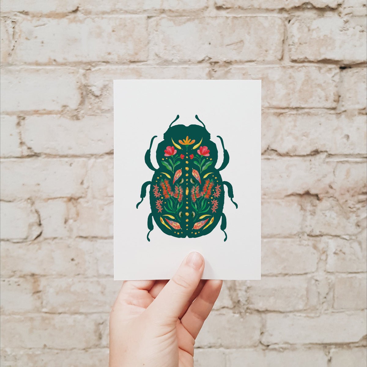 Hand holding a card with a beetle design against a brick wall.