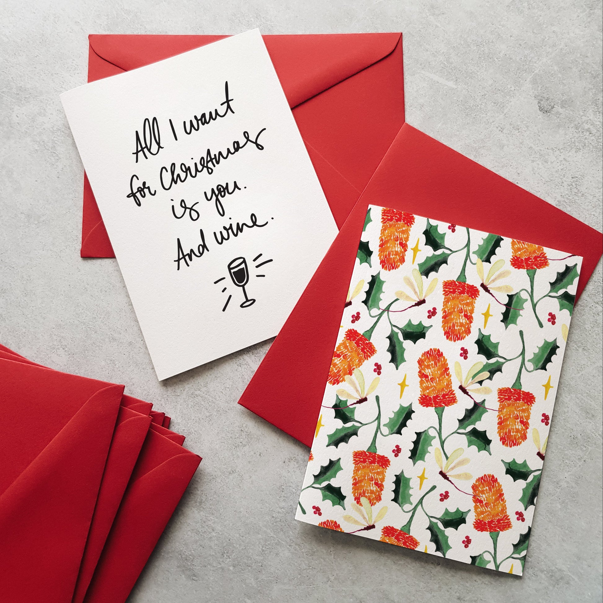 Greeting cards on red envelopes. One greeting card with banksia flowers and the other with black lettering and a wine glass