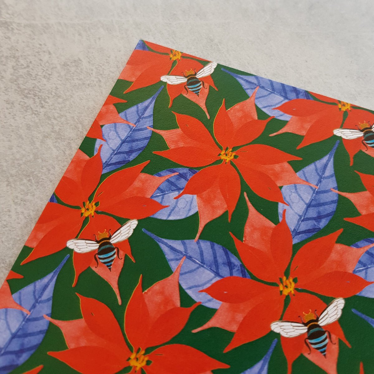 Festive paper with red poinsettias and blue leaves on a textured surface