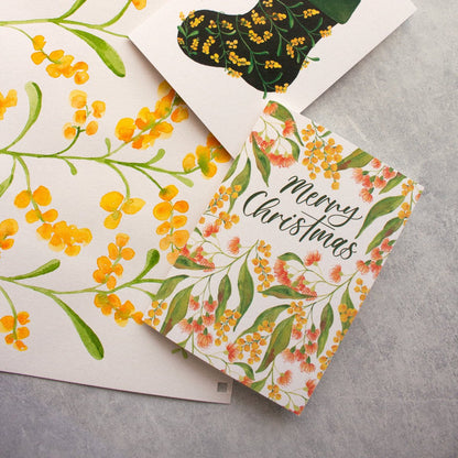 Wattle and flowering gums Christmas card with 'Merry Christmas' text on a grey surface