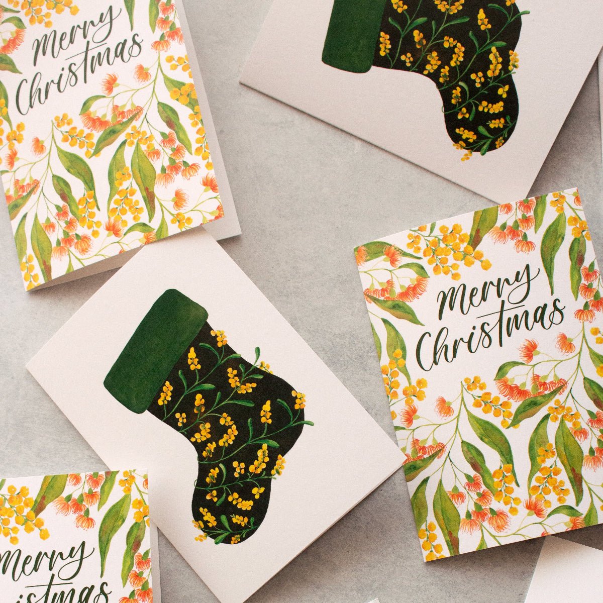 Set of Christmas cards with floral designs and 'Merry Christmas' text on a grey surface.