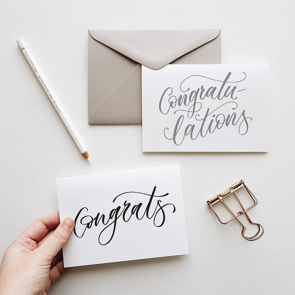 congratulations greeting cards in grey and balck script with a grey envelope surrounded by stationery