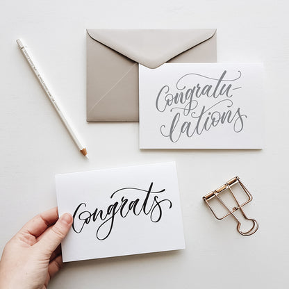 congratulations greeting cards in grey and balck script with a grey envelope surrounded by stationery