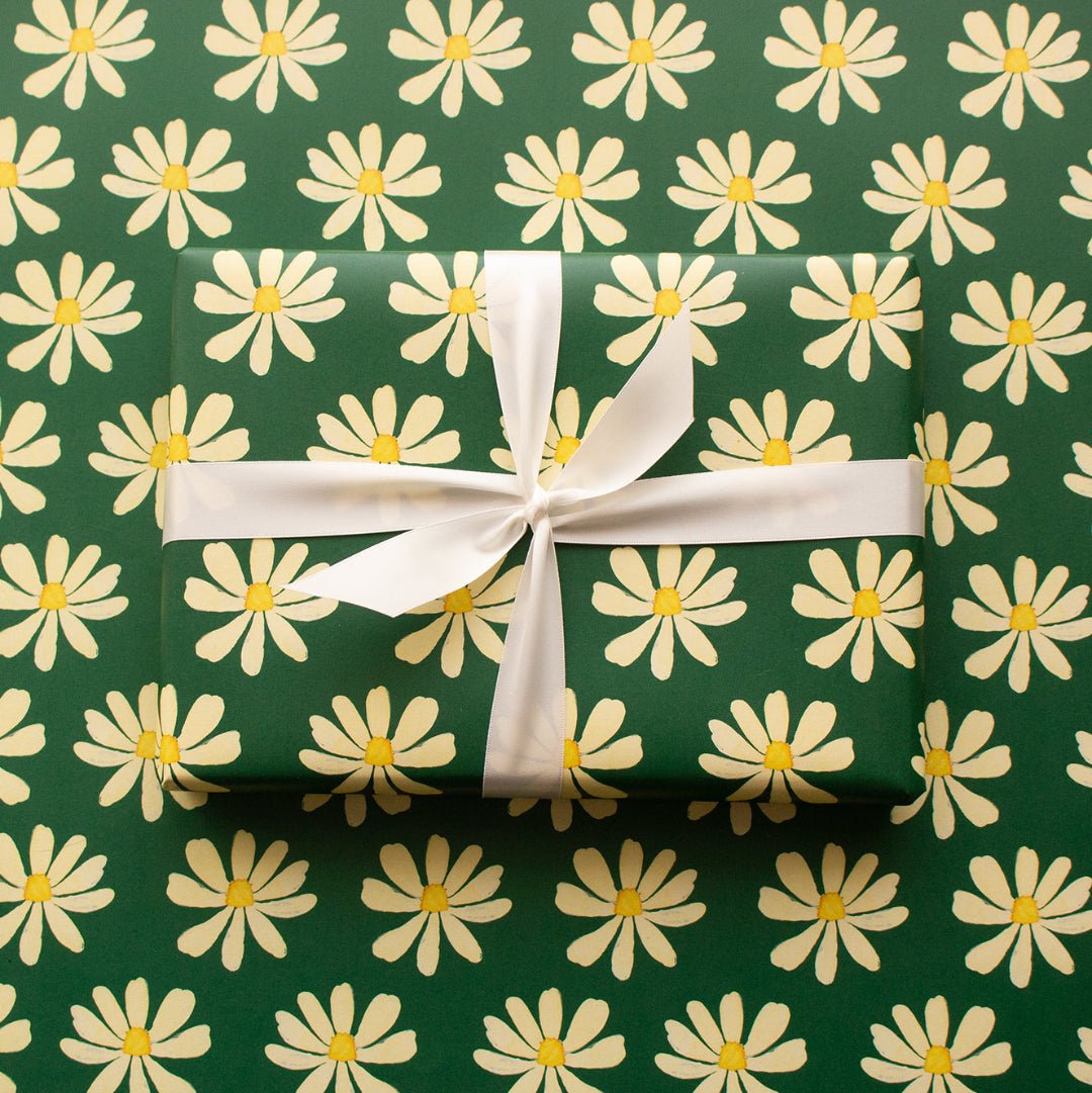 Wrapped present in daisy repeat pattern on a dark green background with white ribbon