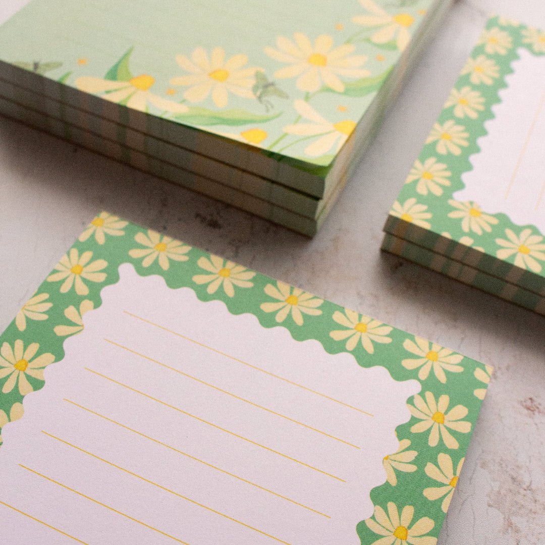 Stacks of green notepads with yellow flower designs on a textured surface