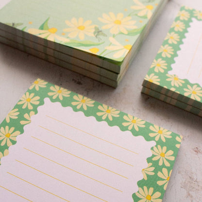 Stacks of green notepads with yellow flower designs on a textured surface