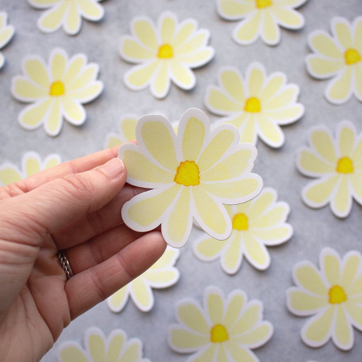 Hand holding a cream flower with a flower repeat in the background 