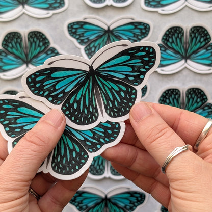 Teal butterfly stickers held by a person with a background of more stickers.