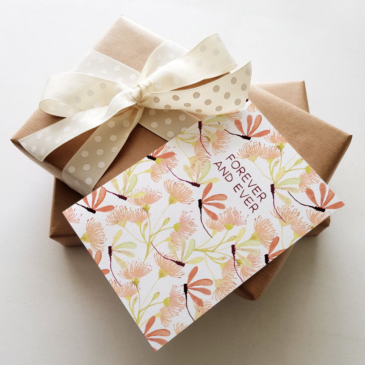Floral greeting card with the words 'FOREVER AND EVER' and dragonfly illustrations, placed on top of two wrapped gift boxes.
