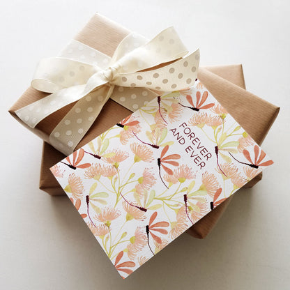 Floral greeting card with the words 'FOREVER AND EVER' and dragonfly illustrations, placed on top of two wrapped gift boxes.