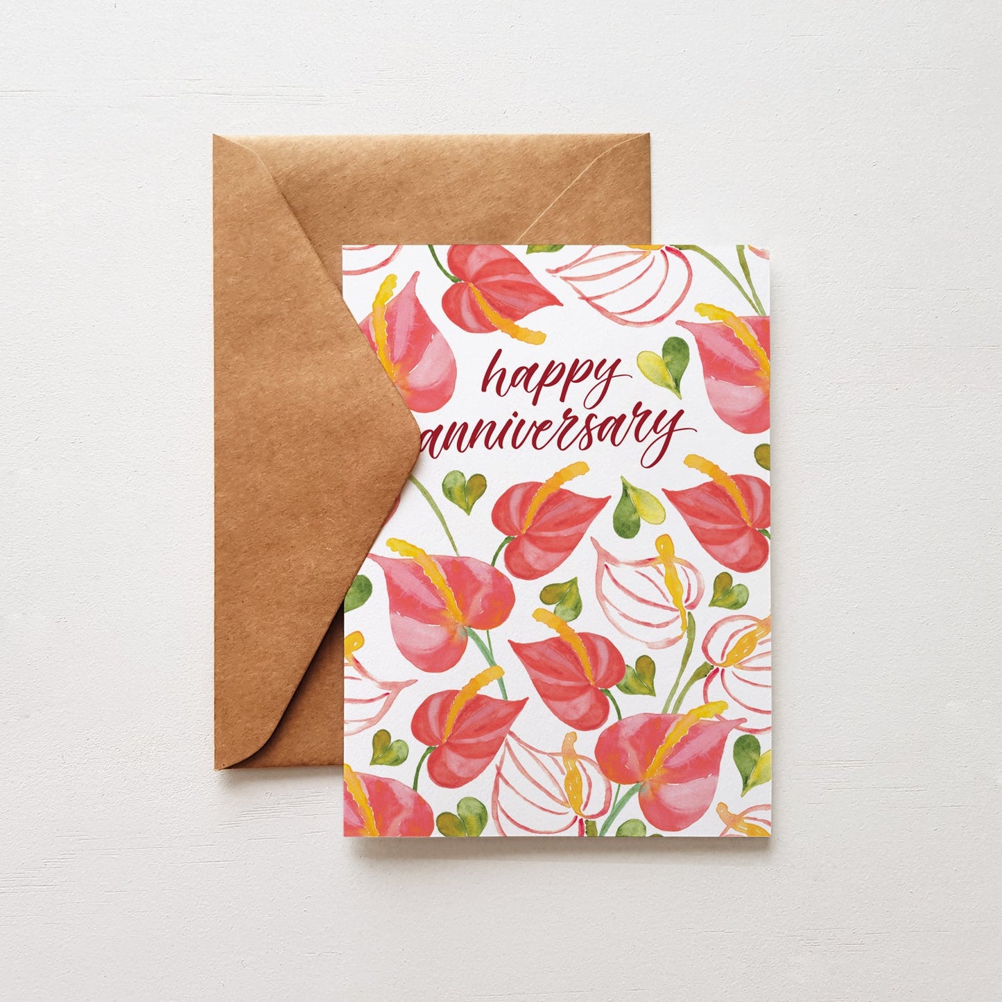 Happy anniversary greeting card with red flowers and a brown envelope on a white background
