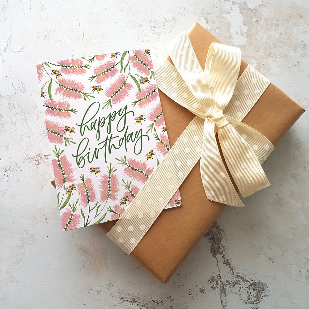 Pink floral Happy Birthday card on a present wrapped in brown paper with a white cream ribbon