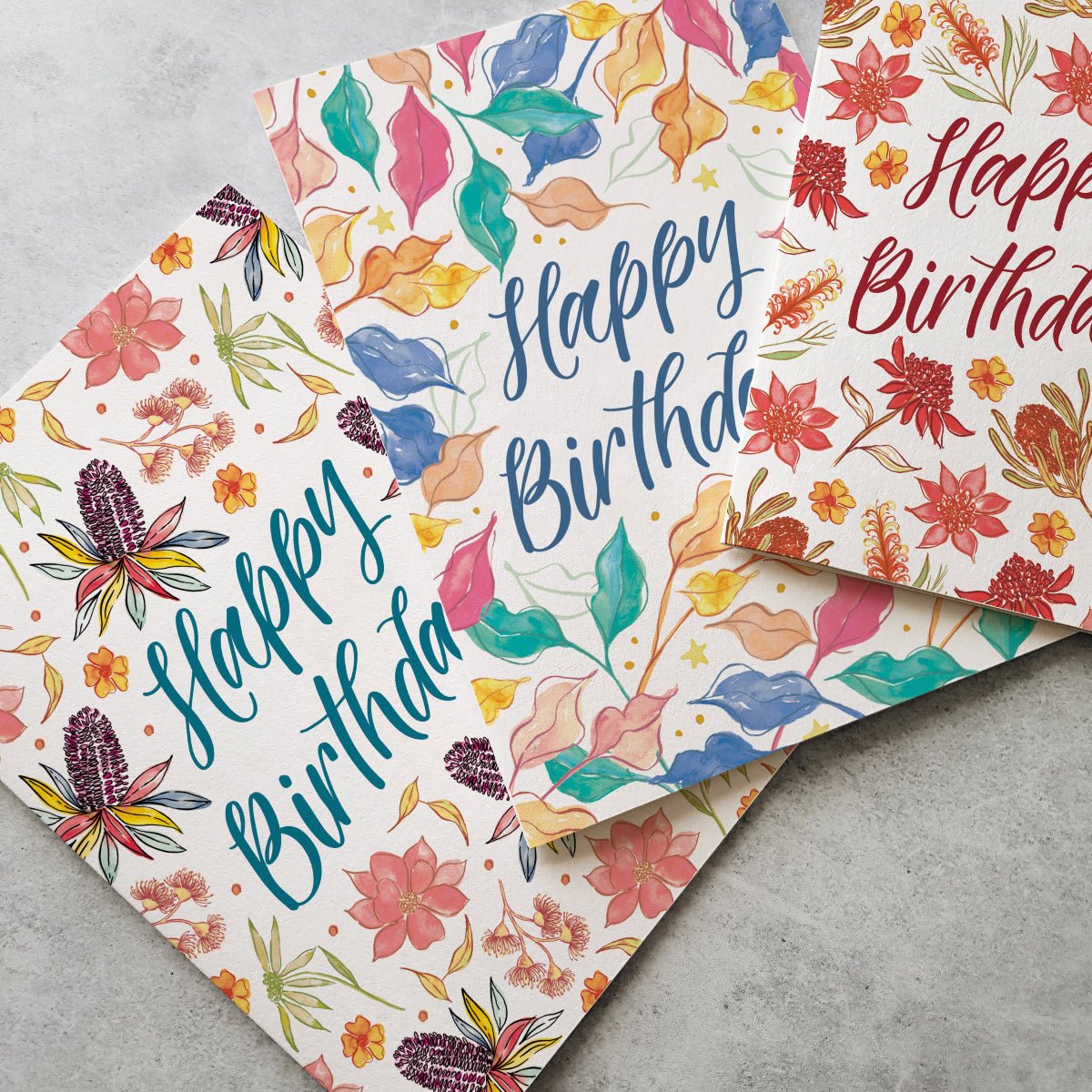 Two colorful birthday cards with floral designs and 'Happy Birthday' text on a gray surface.