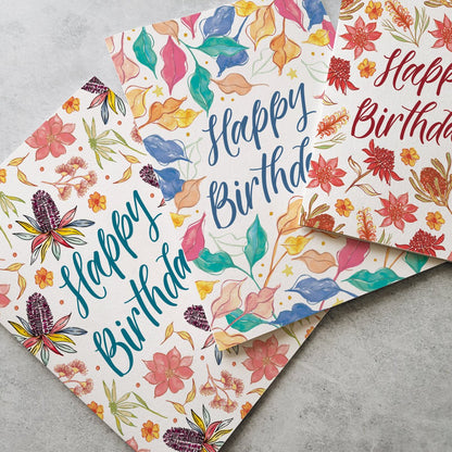 Two colorful birthday cards with floral designs and 'Happy Birthday' text on a gray surface.