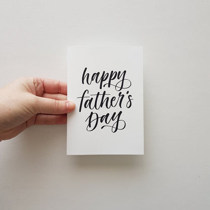Hand holding happy father's day greeting card in black script on a white background